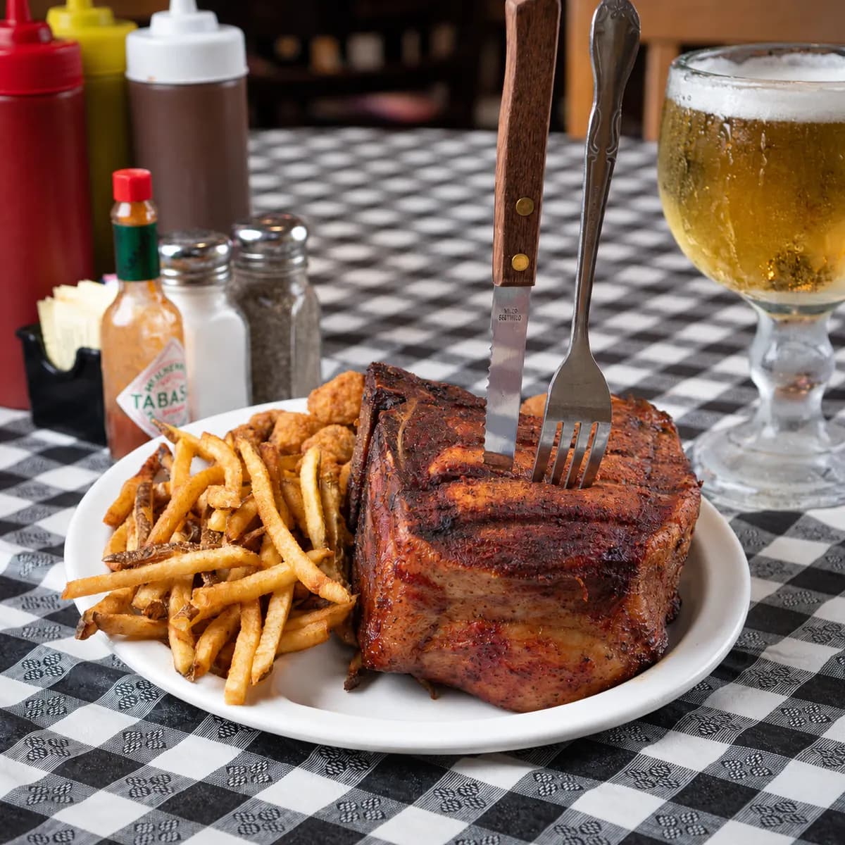 A thick smoked pork chop with hand-cut fries, a knife and fork standing in it at Sammies Bar-B-Q in Fort Worth, TX