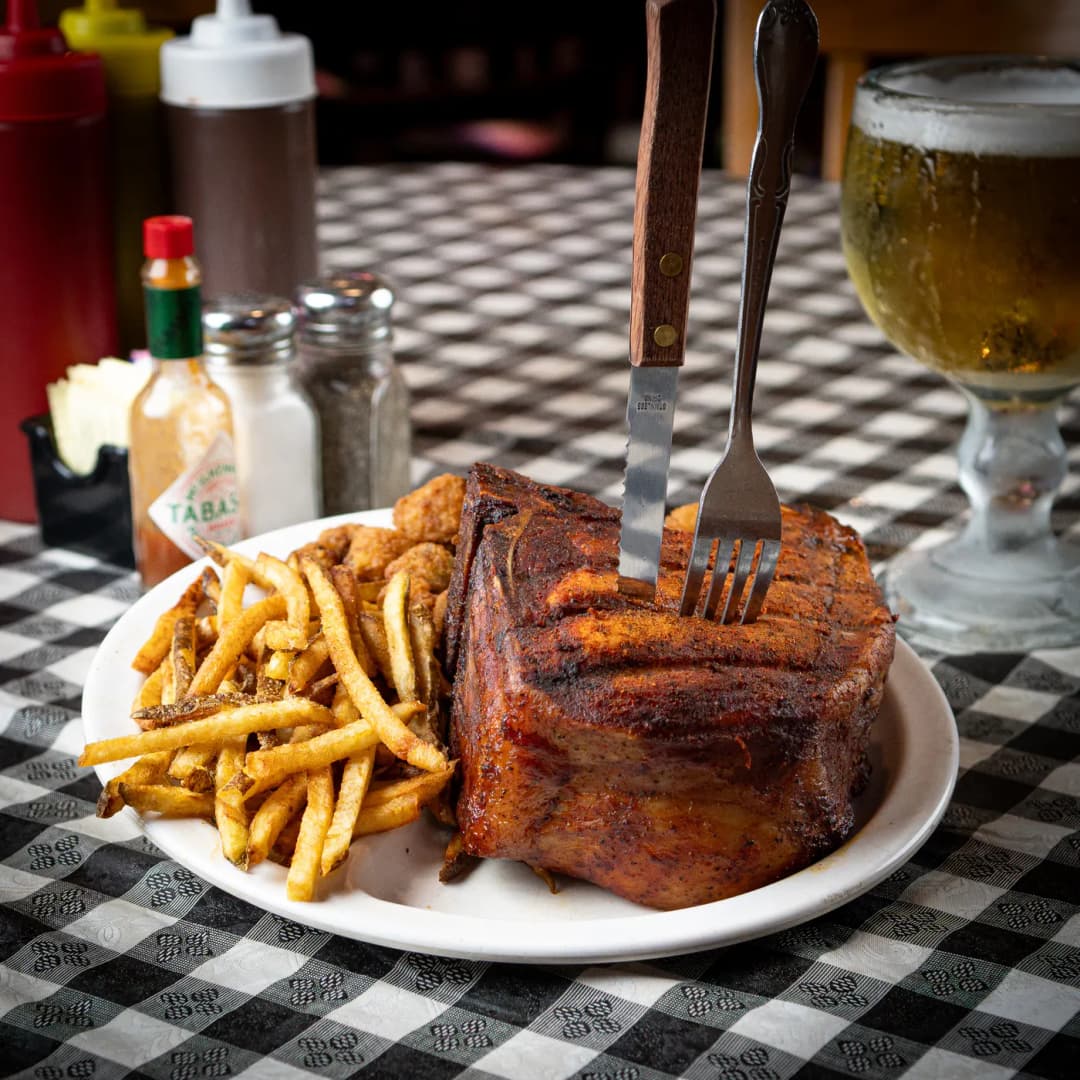 A thick smoked pork chop with hand-cut fries, a fork standing in the meat at Sammies Bar-B-Q in Fort Worth, TX