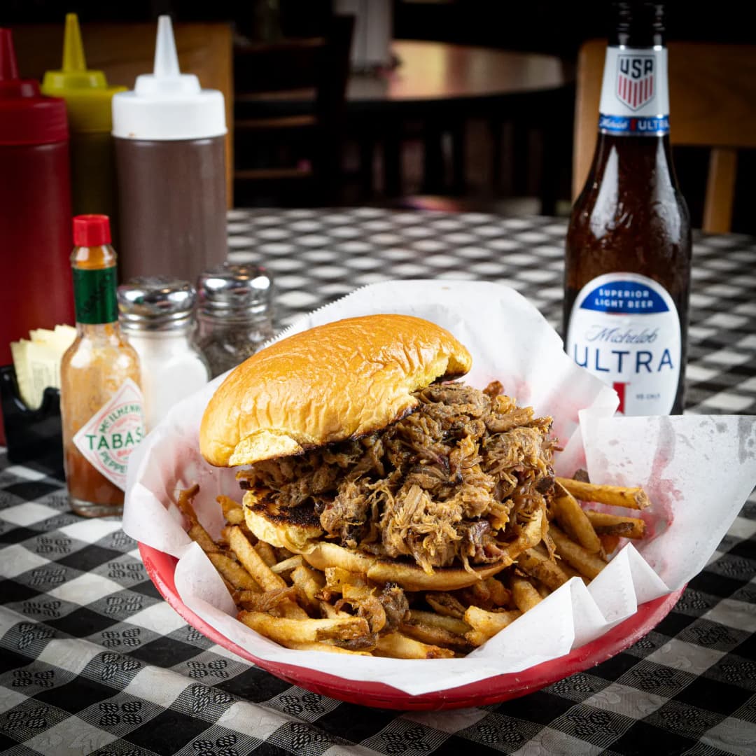 A pulled pork sandwich piled high in a basket with hand-cut fries at Sammies Bar-B-Q in Fort Worth, TX