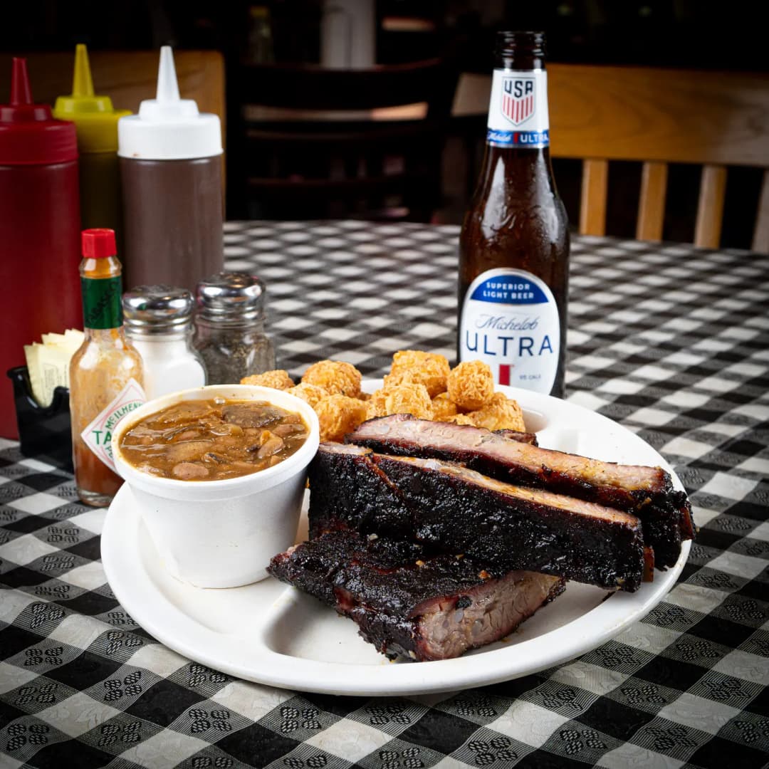 Smoked pork ribs on a plate with tater tots and a cup of beans at Sammies Bar-B-Q in Fort Worth, TX